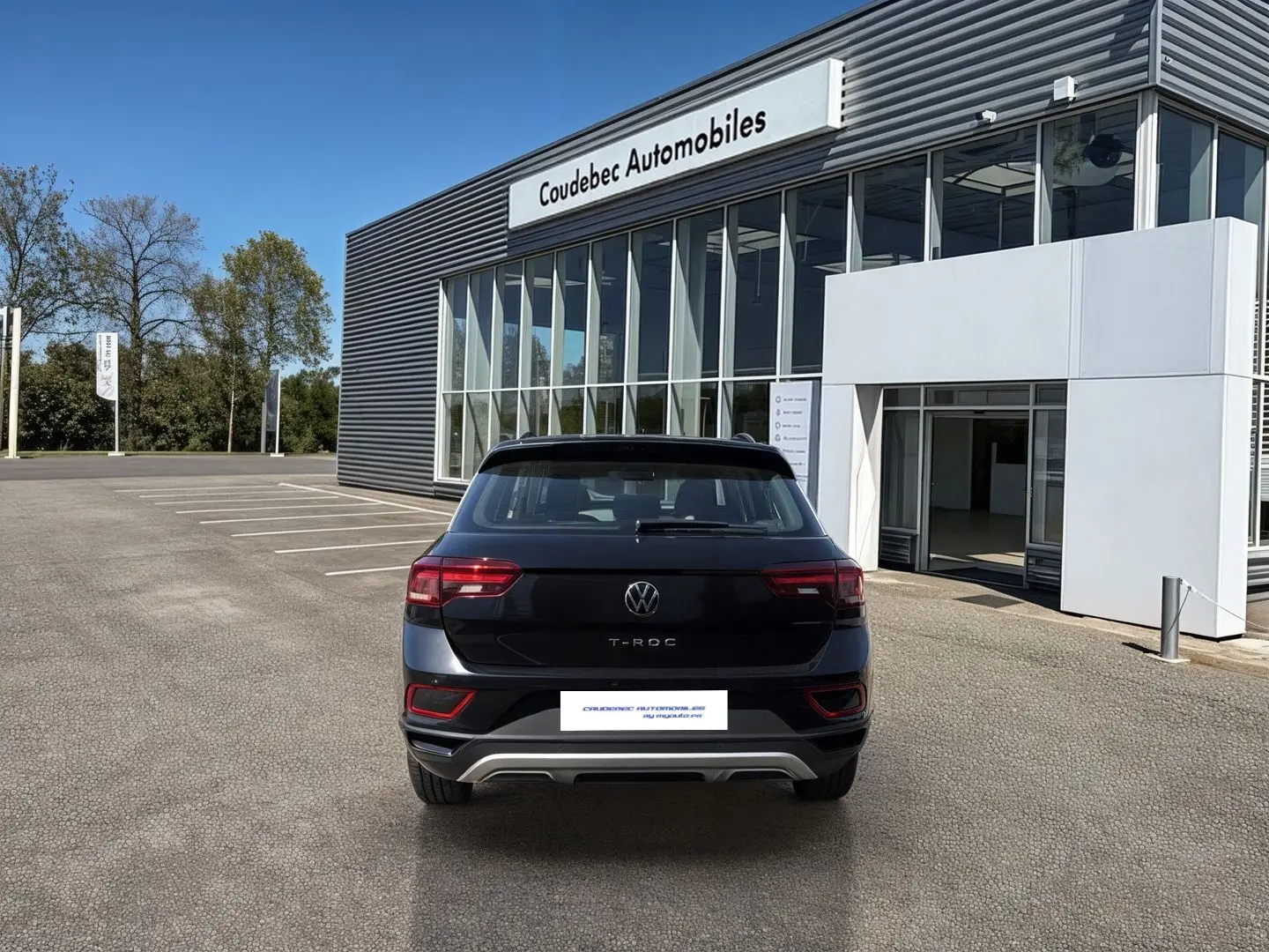 Vue arrière d'un Volkswagen T-Roc noir stationné devant un bâtiment moderne de concession automobile.