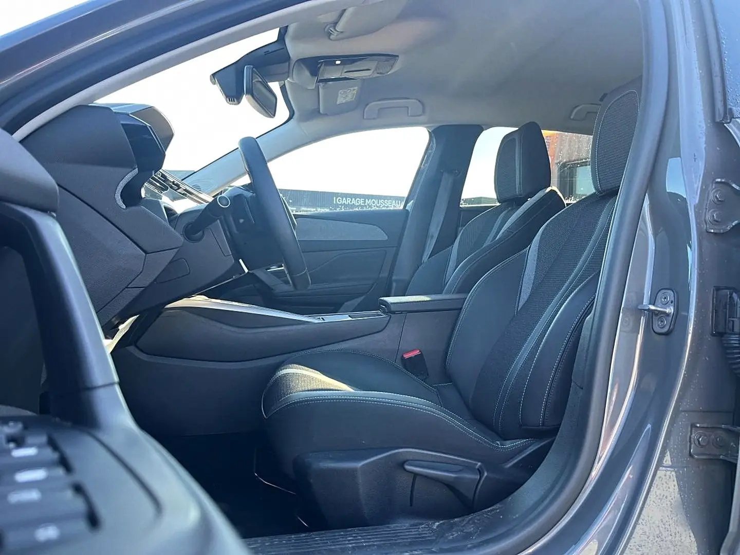 Vue intérieure côté conducteur de la Peugeot 308 gris selenium, montrant les sièges avant et le volant multifonction.