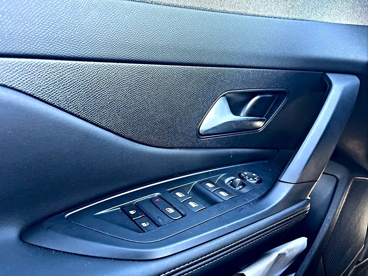 Gros plan sur la porte côté gauche intérieure noire de la Peugeot 308 1.5 BlueHDi 130 avec commandes des vitres et poignée.
