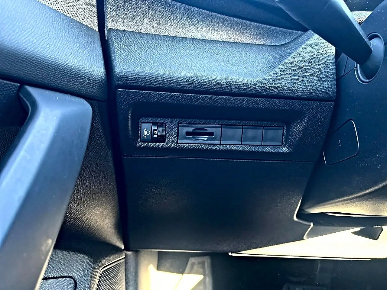 Détail du tableau de bord côté gauche en plastique noir avec commande de réglage des phares sur Peugeot 308 2025.