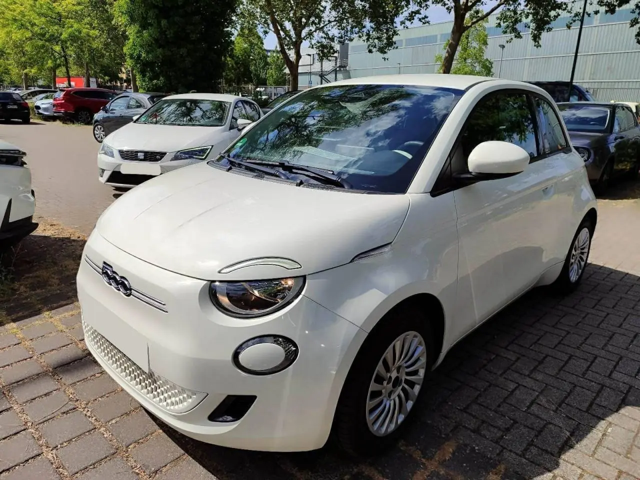 Fiat 500 électrique blanche vue 3/4 avant droit, avec phares ronds et calandre épurée distinctive.