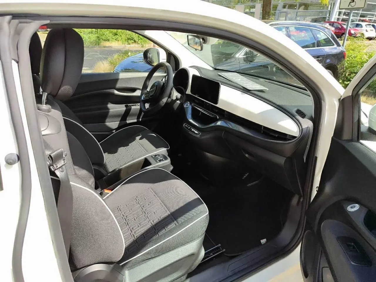 Intérieur de la Fiat 500 électrique 2024 vue côté conducteur, sièges noirs avec surpiqûres blanches et tableau de bord blanc.