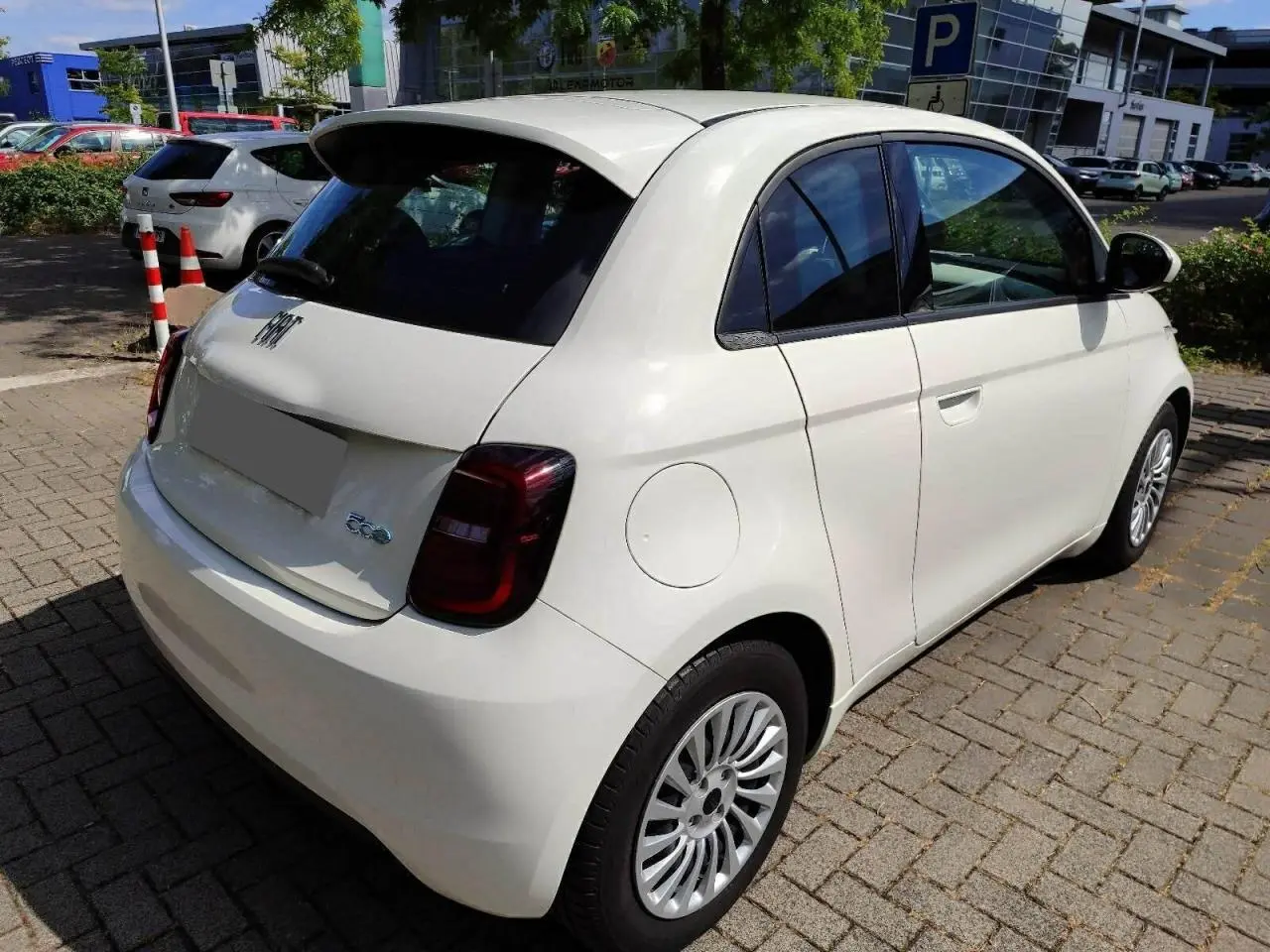 Fiat 500 électrique blanche vue 3/4 arrière droit, avec feux arrière foncés et jantes multibranches.
