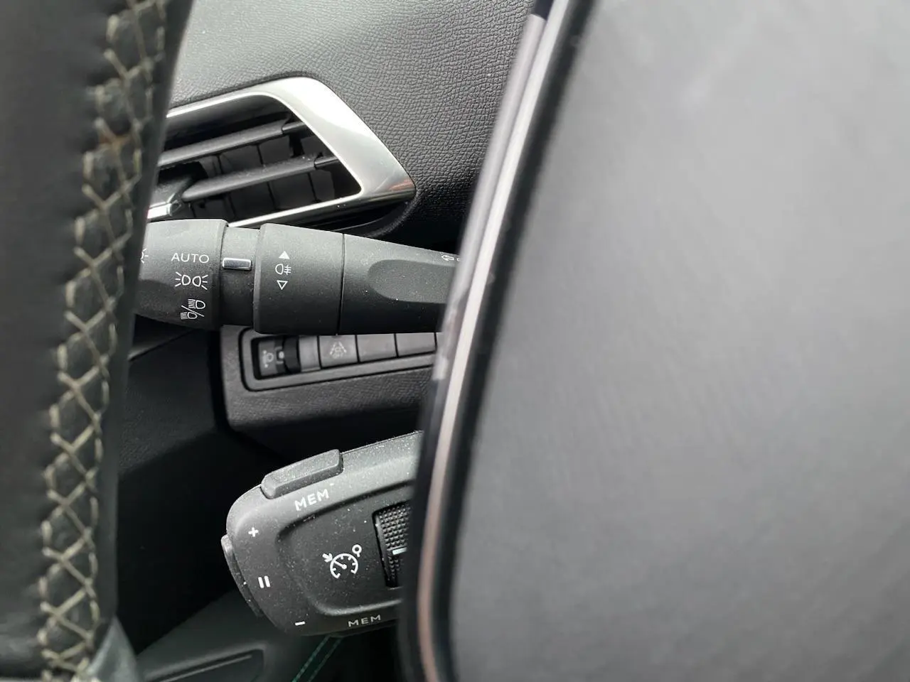 Détail du commodo de régulateur de vitesse et des commandes d'éclairage à gauche du volant dans un Peugeot 3008 gris platinium.