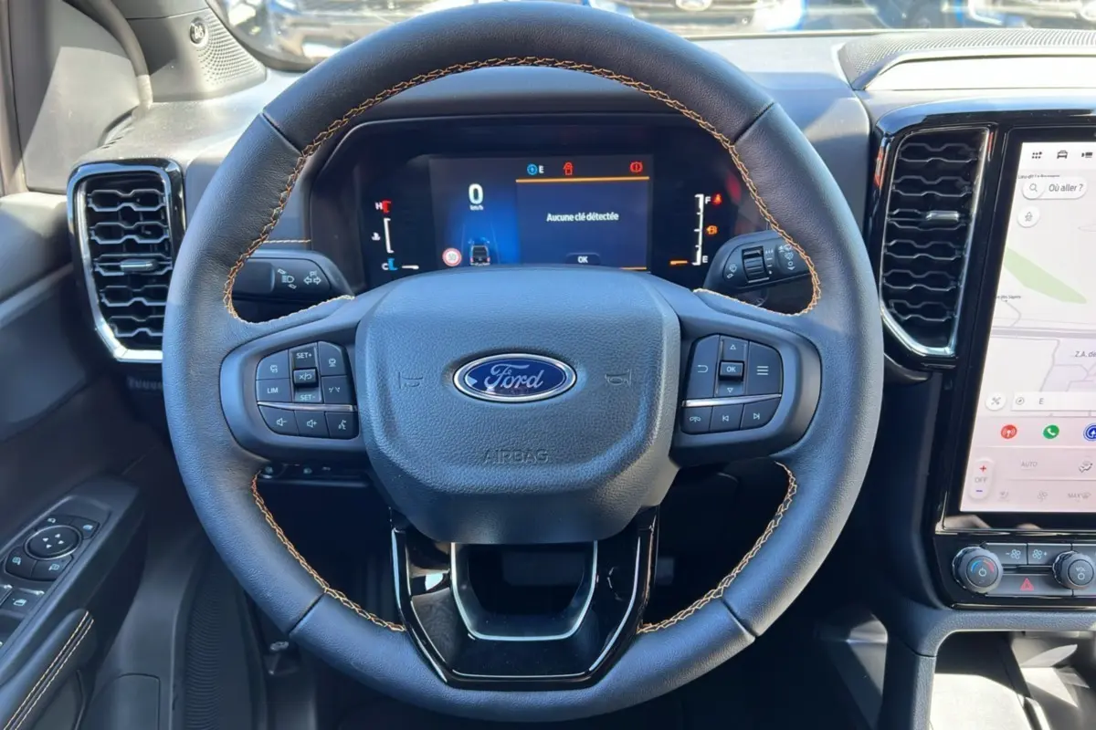 Vue rapprochée du volant en cuir avec surpiqûres marron du Ford Ranger 3.0 V6 240 Wildtrak Plus gris carbone, tableau de bord digital visible.