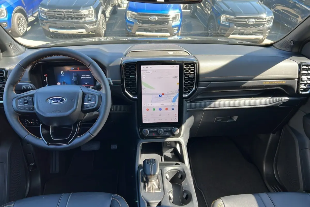 Vue intérieure du Ford Ranger 2025 gris carbone, version Wildtrak Plus, avec tableau de bord moderne et écran tactile vertical central.