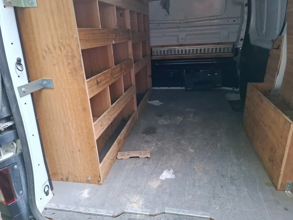 Intérieur du fourgon blanc Renault Trafic L1H1 2021 vu de l'arrière, avec aménagements en bois sur les côtés.