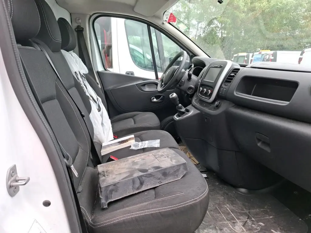 Intérieur du Renault Trafic Fourgon blanc vu côté conducteur, montrant les sièges noirs et le tableau de bord moderne.