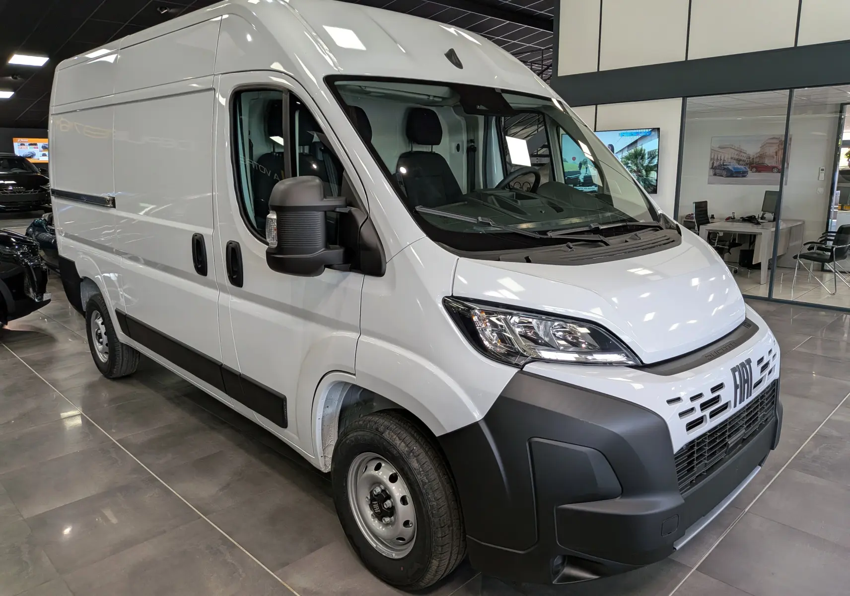 Fiat Ducato Fourgon blanc en vue 3/4 avant droit, avec calandre noire et rétroviseurs larges visibles en intérieur showroom.