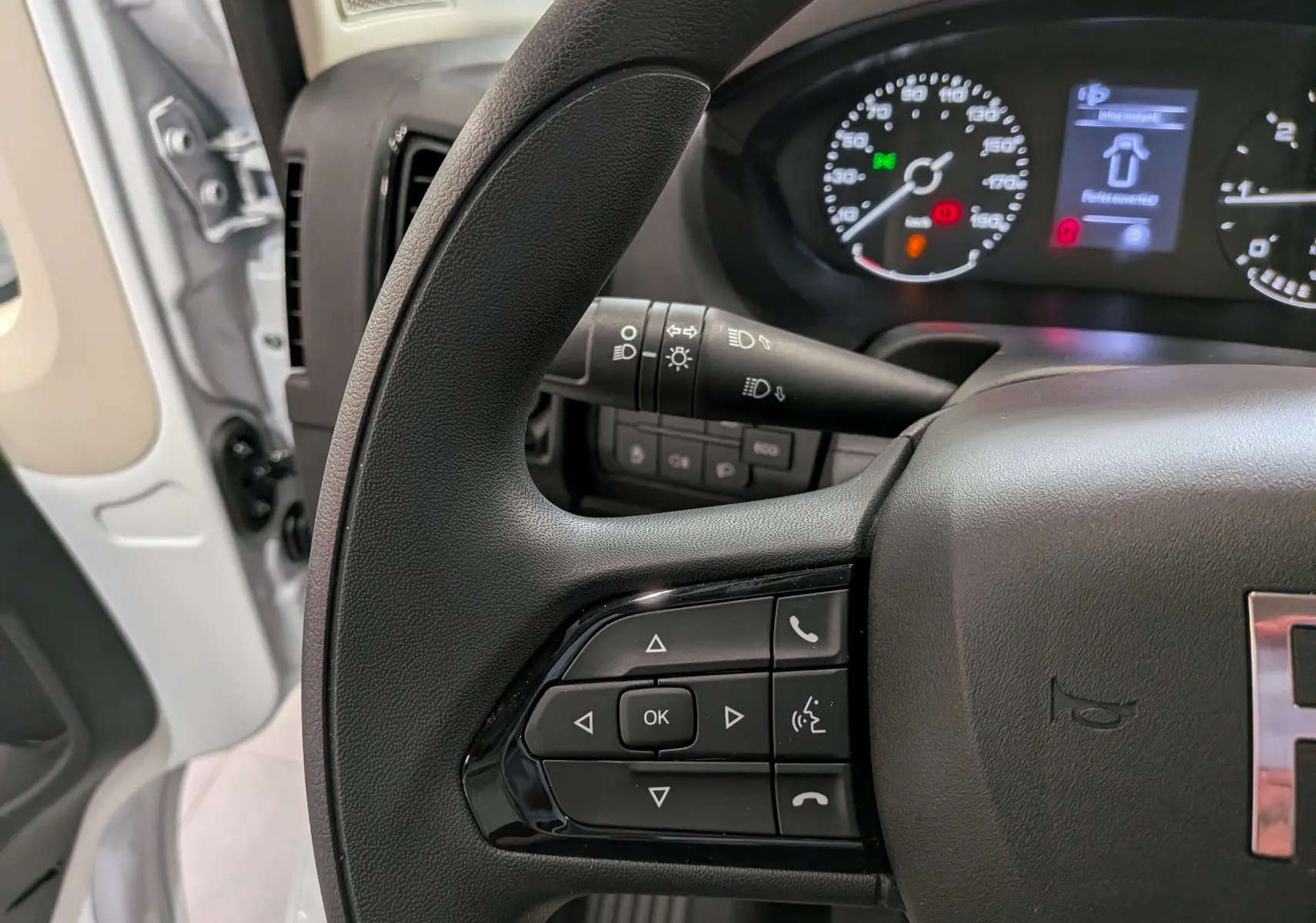 Gros plan sur le volant noir du Fiat Ducato Fourgon blanc 2026, avec commandes multifonctions et tableau de bord lumineux en arrière-plan.