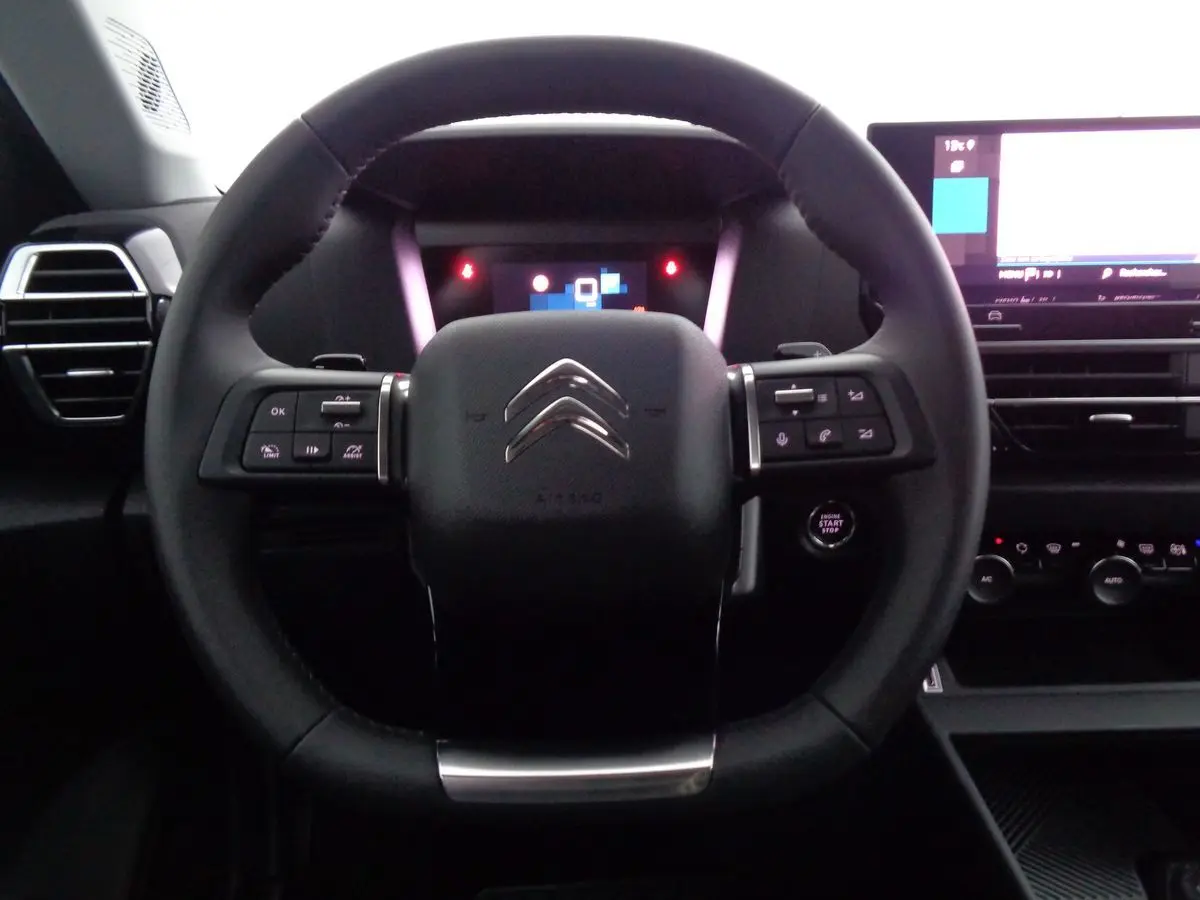 Vue intérieure centrée sur le volant noir du Citroën C4 2023 avec commandes intégrées et tableau de bord digital.