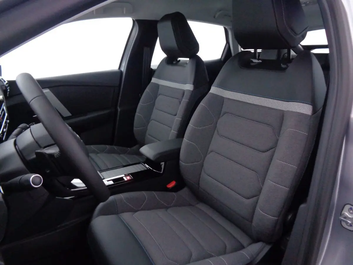 Intérieur de la Citroën C4 2023, vue côté conducteur, sièges tissu gris avec surpiqûres bleues et accoudoir central.