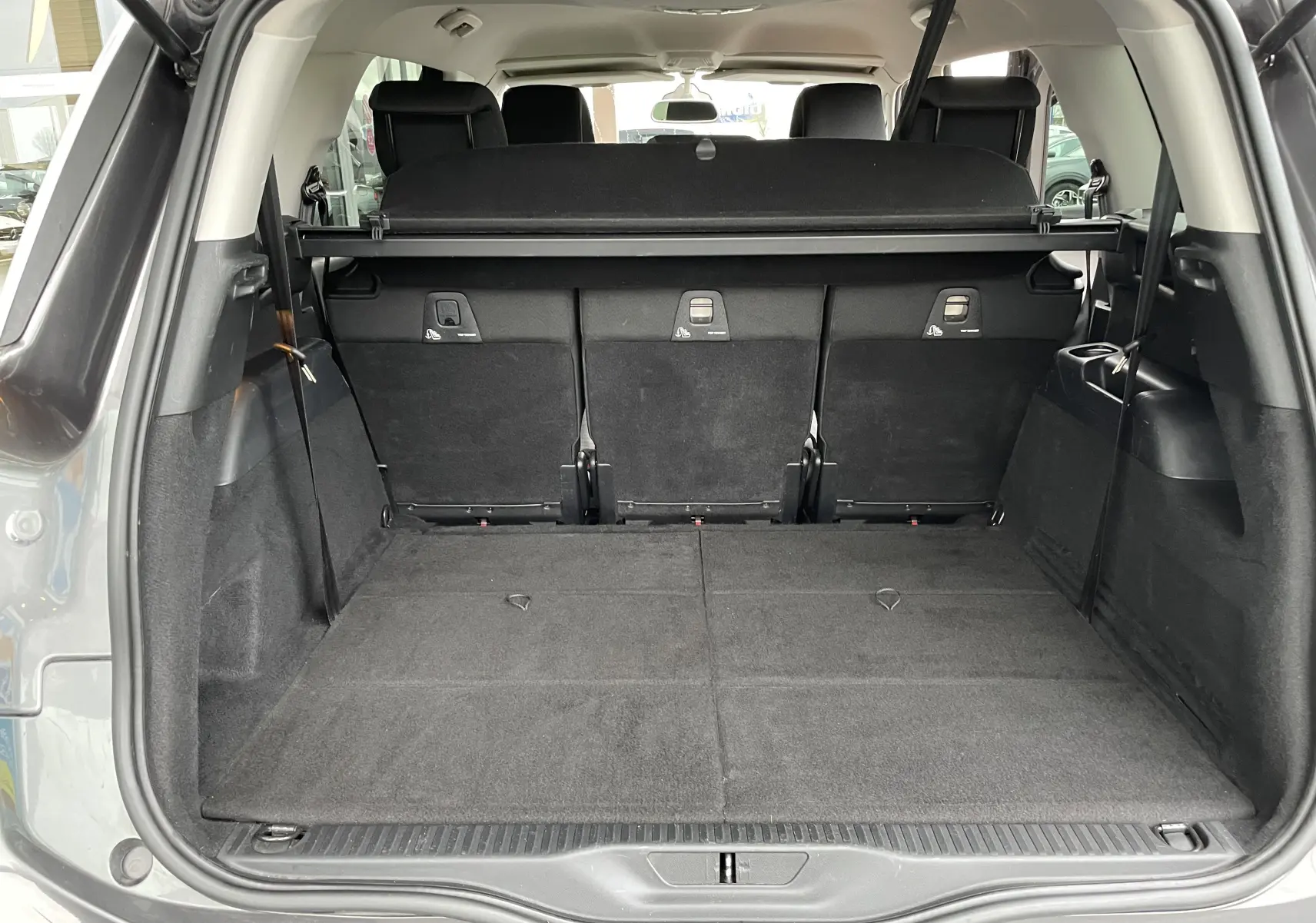 Coffre ouvert du Citroën Grand C4 Picasso gris, vue arrière montrant les sièges rabattus et l'espace de chargement spacieux.