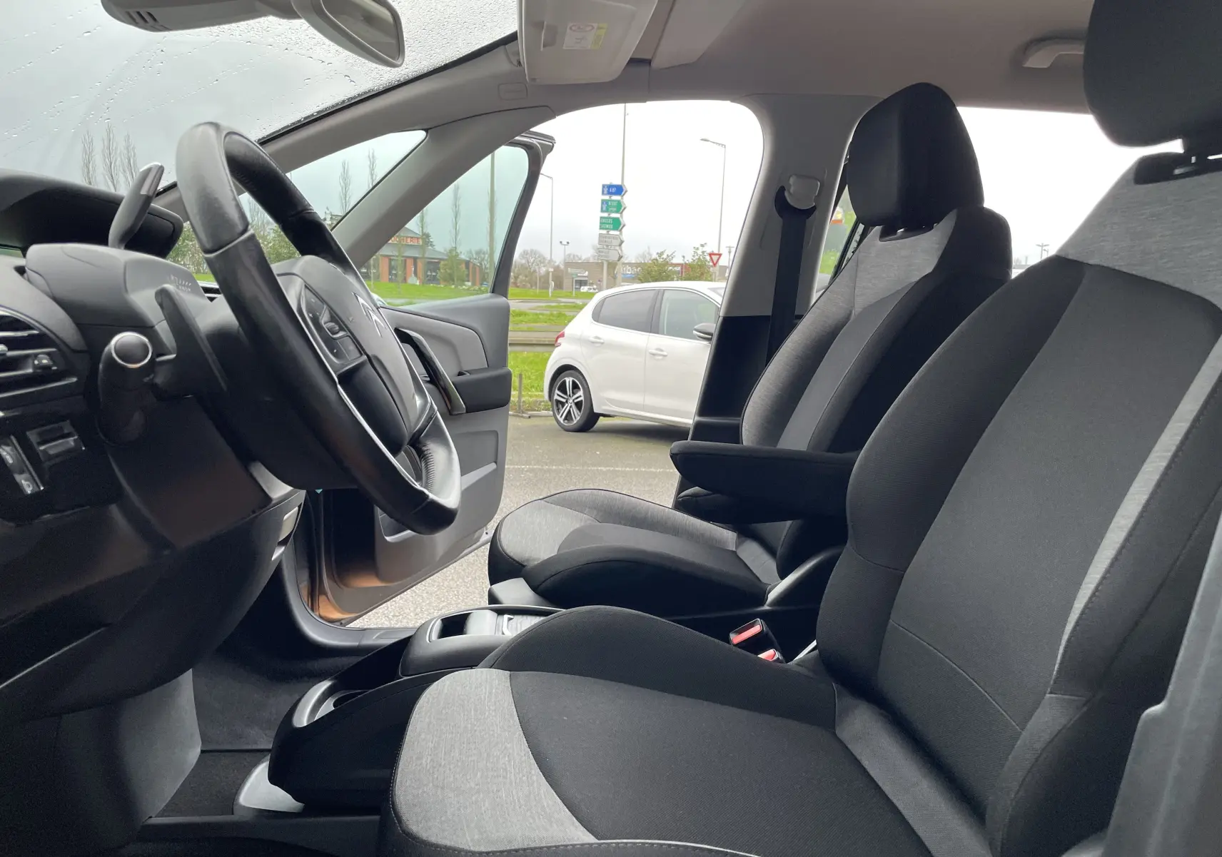 Intérieur avant du Citroën Grand C4 Picasso gris 2018, sièges tissu bicolore et volant multifonction visible côté conducteur.