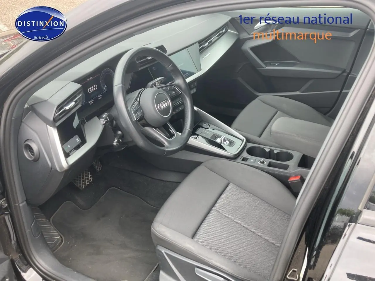 Vue intérieure côté conducteur de l'Audi A3 Sportback noire, mettant en valeur le volant cuir multifonction et la console centrale moderne.