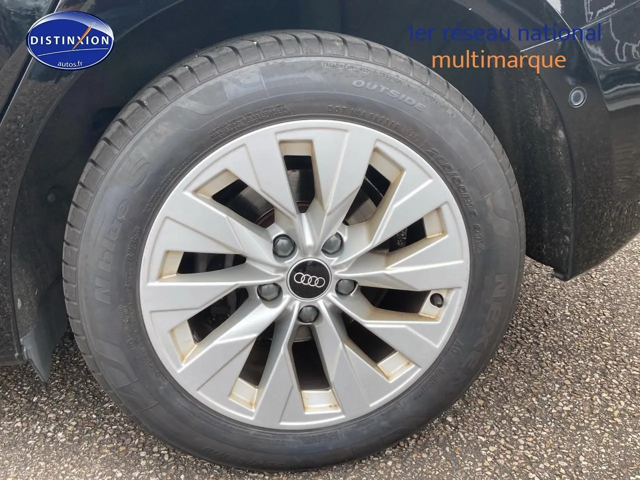 Gros plan sur la jante alu argentée avec logo Audi d'une Audi A3 Sportback noire, côté avant droit.