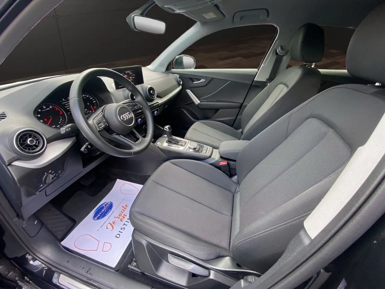 Vue intérieure côté conducteur de l'Audi Q2 35 TFSI S-Line 2023 avec sièges tissu noir et tableau de bord moderne.