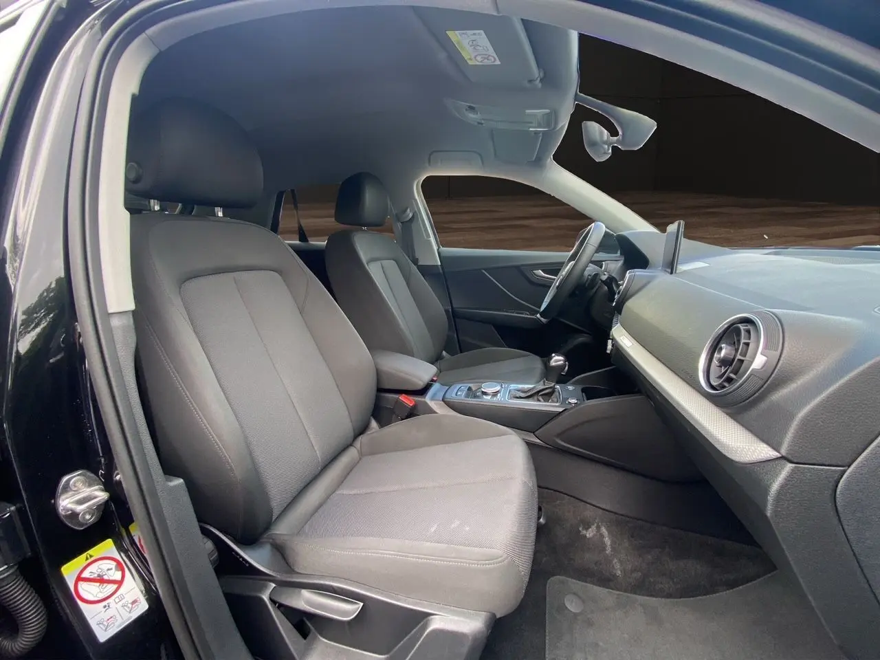 Intérieur noir de l'Audi Q2 2023 vu côté conducteur, avec sièges tissu et tableau de bord moderne.