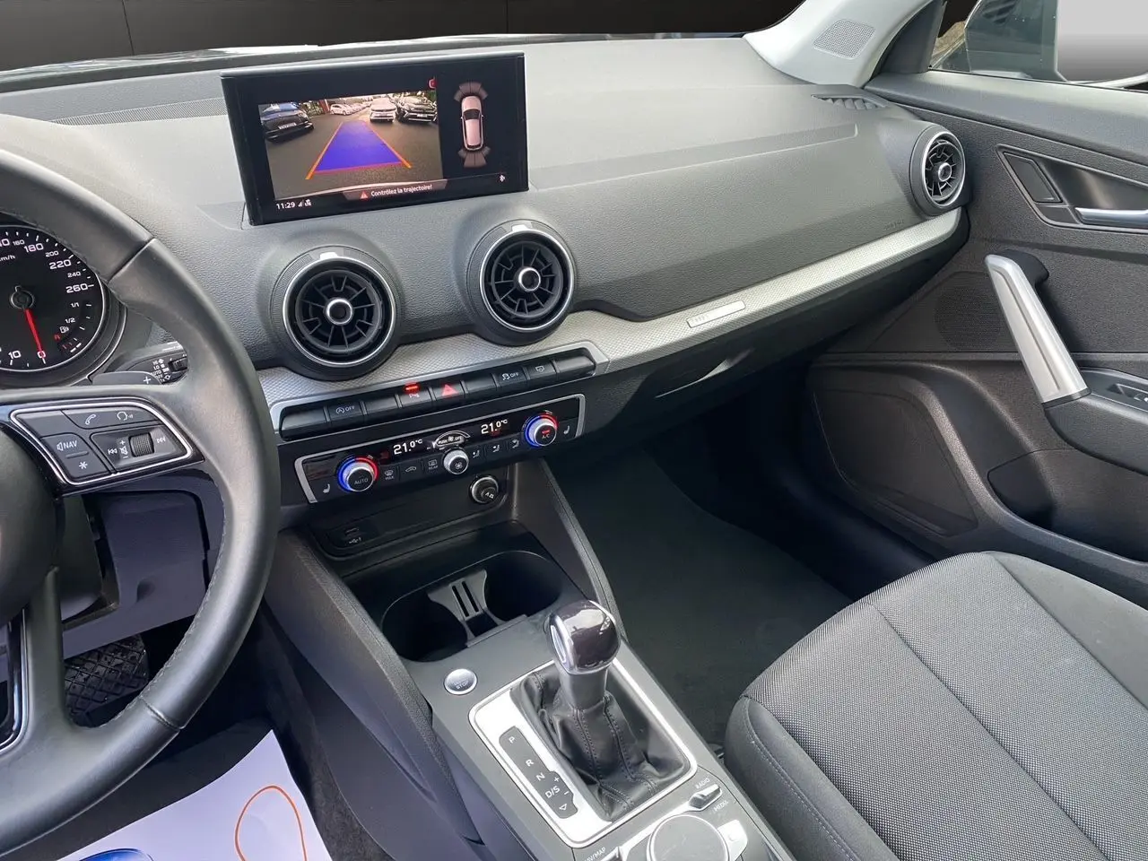 Vue intérieure de l'Audi Q2 35 TFSI 2023 montrant le tableau de bord noir avec écran caméra de recul et console centrale.