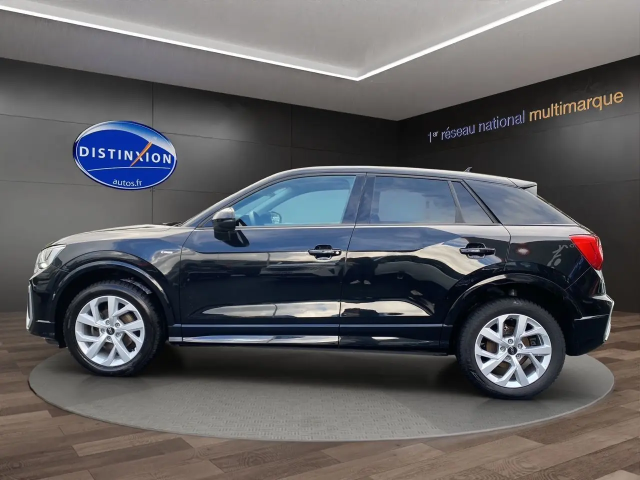 Audi Q2 noir mito vue de profil côté gauche, avec jantes alliage 17 pouces et hayon motorisé visible en arrière-plan.