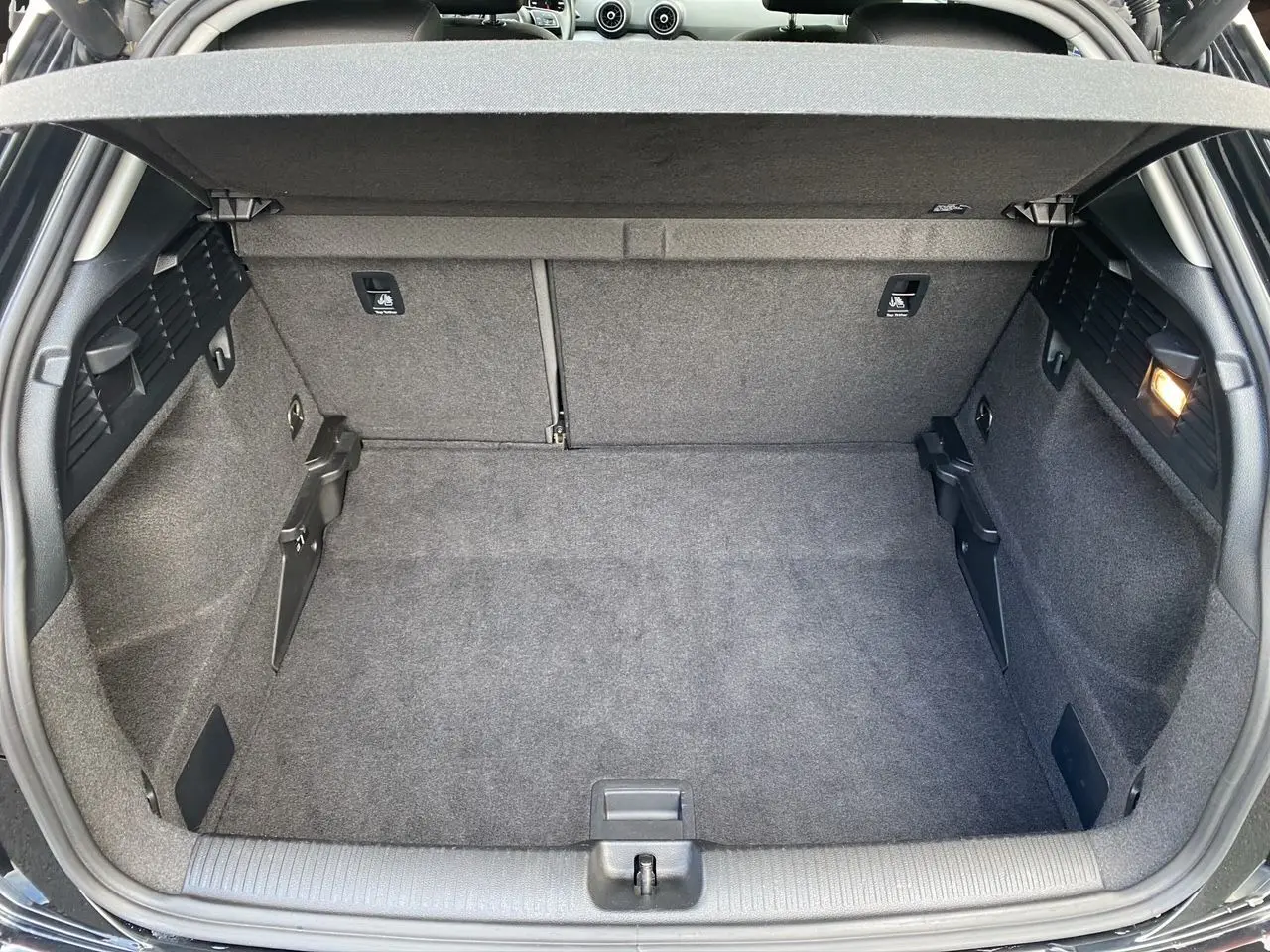 Coffre spacieux de l'Audi Q2 noir mito, vue intérieure arrière avec revêtement gris et éclairage latéral allumé.