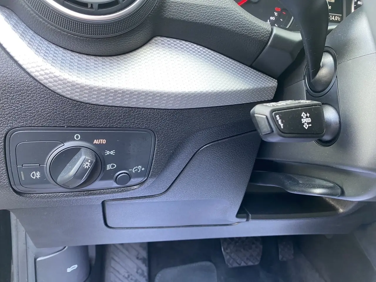 Détail du tableau de bord noir de l'Audi Q2 2023 montrant la commande des phares et le levier de régulateur de vitesse.