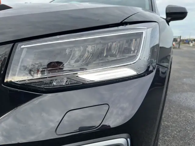 Gros plan sur le phare avant droit noir mito d'un Audi Q2 35 TFSI S-Line 2023 avec détails LED et carrosserie brillante.