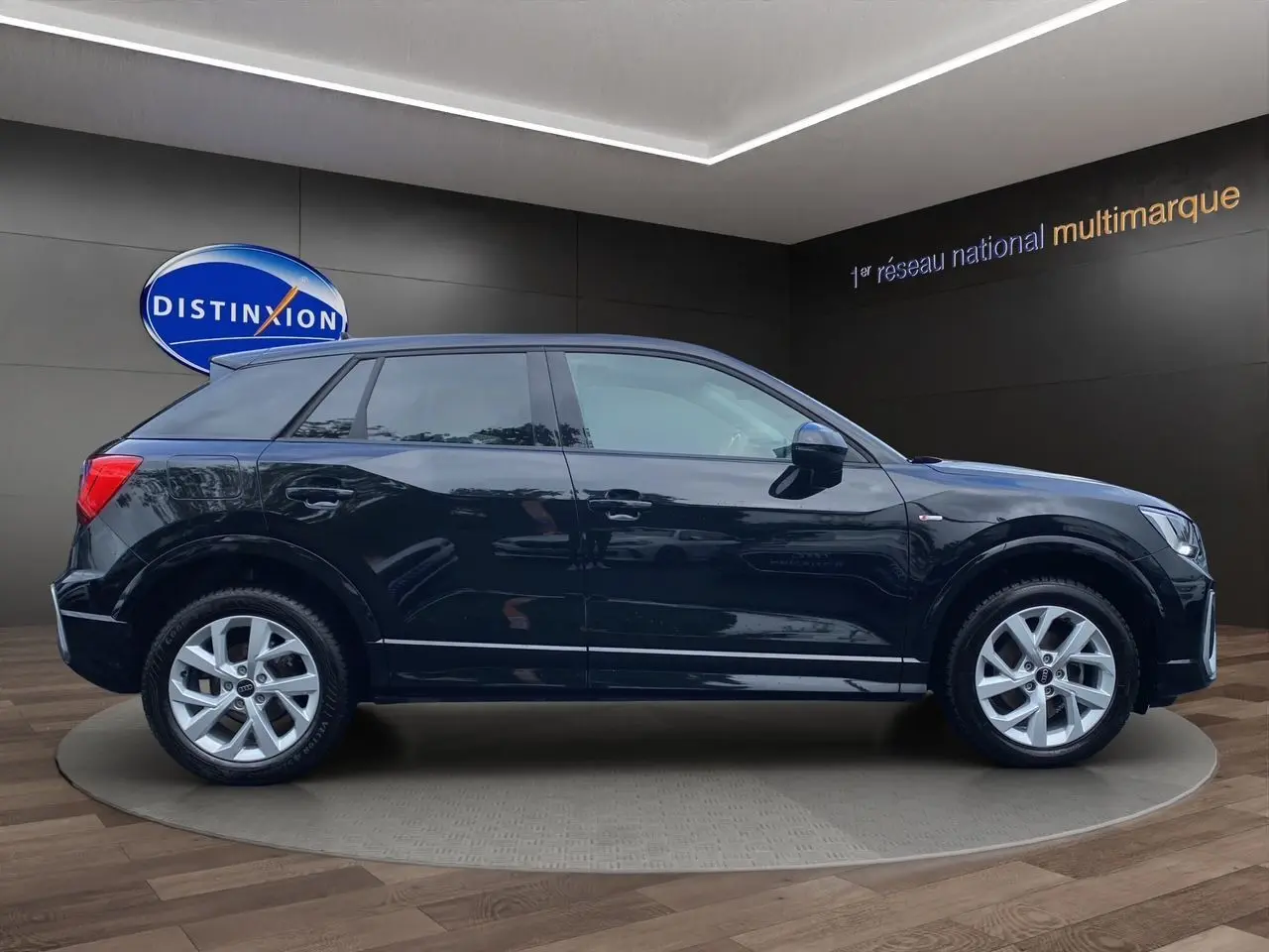 Profil côté gauche d'un Audi Q2 noir mito 2023 avec jantes alliage 17 pouces et hayon motorisé visible en showroom.
