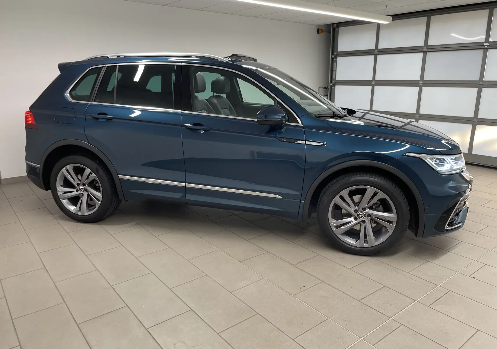 Volkswagen Tiguan 2024 bleu Nightshade en vue profil côté gauche, avec jantes alliage et attelage escamotable visible.