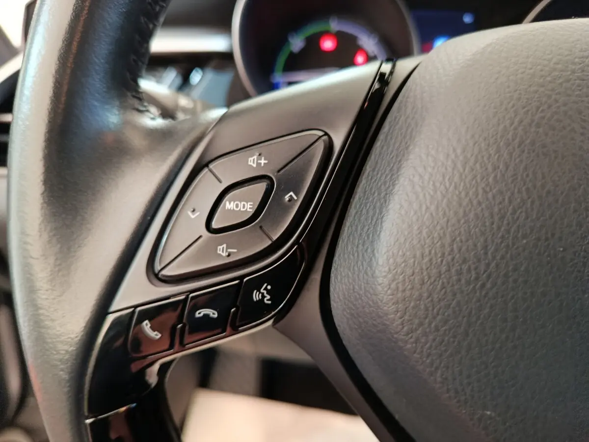 Gros plan sur les commandes gauche du volant cuir noir du Toyota C-HR gris clair, avec boutons mode et appels.
