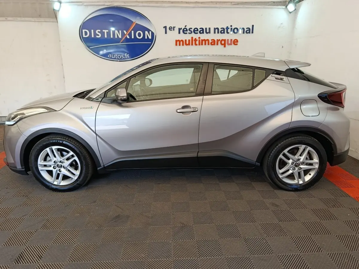 Profil côté gauche d'un Toyota C-HR gris clair hybride 2022, avec jantes alliage et lignes anguleuses distinctives.