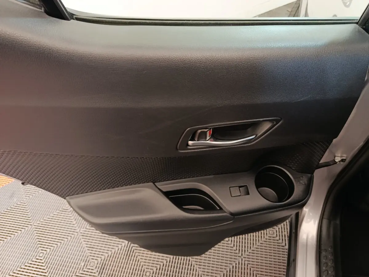 Vue intérieure côté gauche de la porte avant grise claire du Toyota C-HR 2.0 Hybride avec poignée et porte-gobelet.