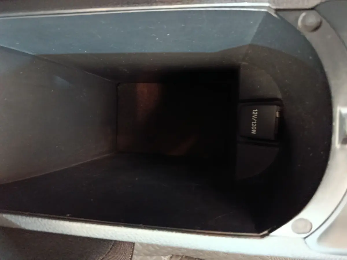 Vue intérieure du compartiment de rangement central noir avec prise 12V visible dans un Toyota C-HR gris clair.