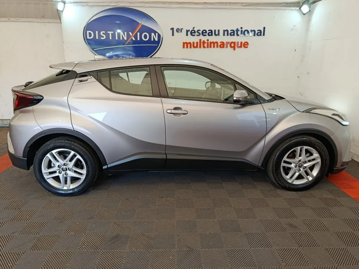Vue latérale droite d'un Toyota C-HR gris clair 2.0 Hybride 184 Dynamic Business Beyond, en intérieur showroom.