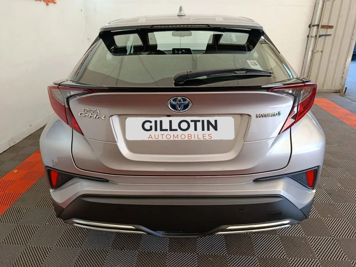 Vue arrière d'un Toyota C-HR gris clair hybride 2022 avec feux arrière anguleux et logo Toyota visible.
