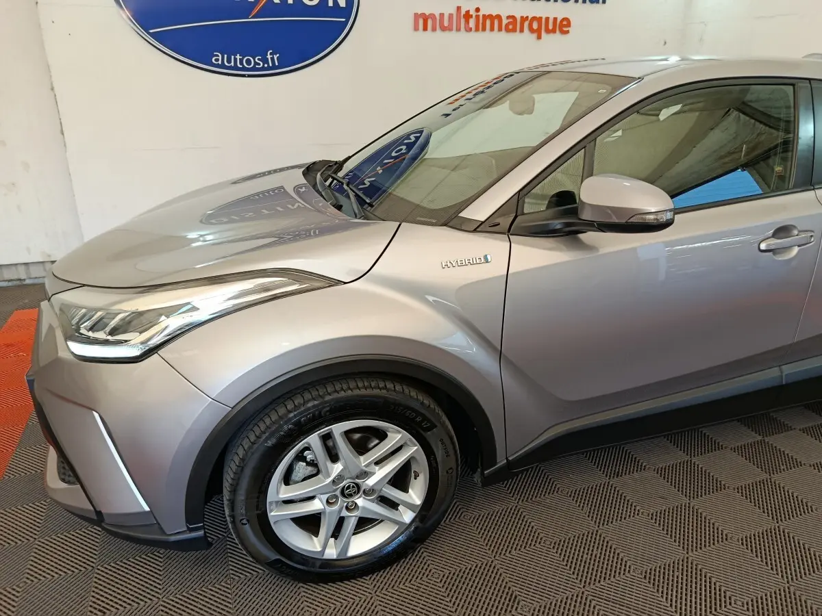 Vue 3/4 avant droit du Toyota C-HR gris clair hybride avec jante alliage et badge Hybrid visible sur l'aile.