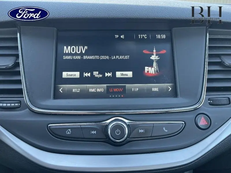 Vue rapprochée de l’écran tactile central et des commandes multimédia de l’Opel Astra 1.5 D blanche, affichant une radio FM.