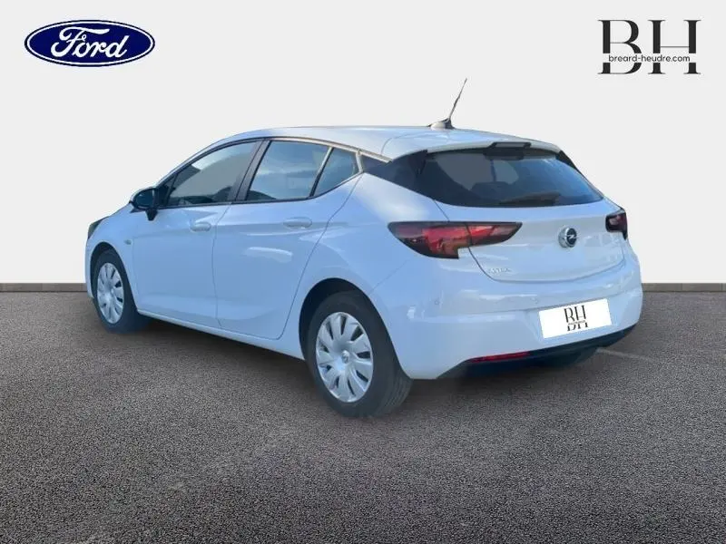 Opel Astra blanc glacier vue 3/4 arrière droit, avec feux arrière foncés et jantes à enjoliveurs simples.