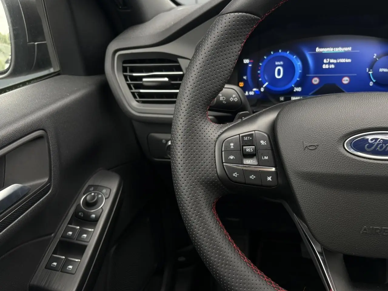 Vue rapprochée du volant perforé noir avec surpiqûres rouges et tableau de bord numérique du Ford Kuga 2023.
