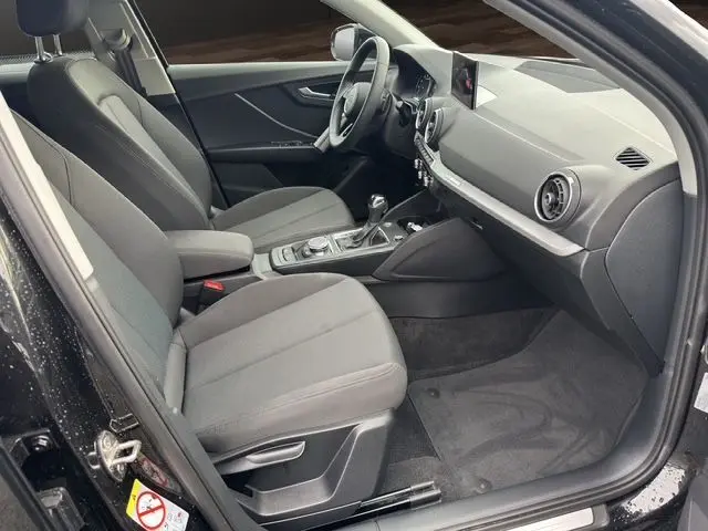 Intérieur noir de l'Audi Q2 35 TFSI 2023 vu côté conducteur, avec sièges tissu et console centrale moderne.