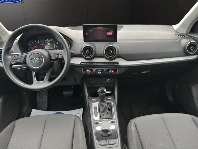 Vue intérieure avant de l'Audi Q2 35 TFSI S-Line 2023 avec tableau de bord noir, volant multifonction et écran central.