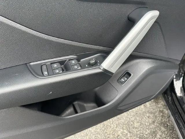 Détail de la porte avant gauche noire de l'Audi Q2 35 TFSI S-Line avec commandes des vitres et poignée argentée.