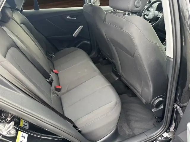Vue intérieure côté gauche des sièges arrière en tissu noir du SUV Audi Q2 noir Mito, avec ceintures de sécurité visibles.