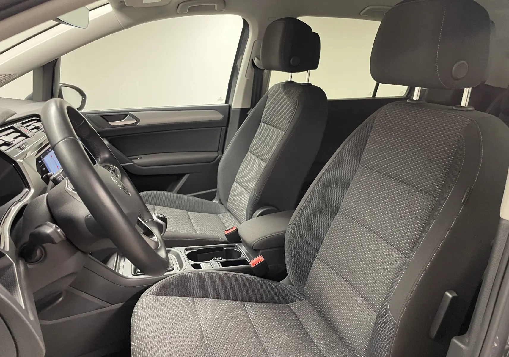 Vue intérieure côté conducteur du Volkswagen Touran 2024, sièges tissu gris et console centrale avec boîte manuelle.