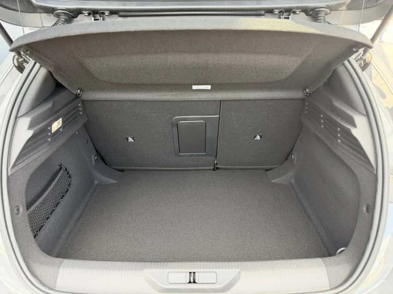 Coffre ouvert vu de l'arrière d'une Peugeot 308 gris Selenium, avec banquette rabattable et filet de rangement latéral.
