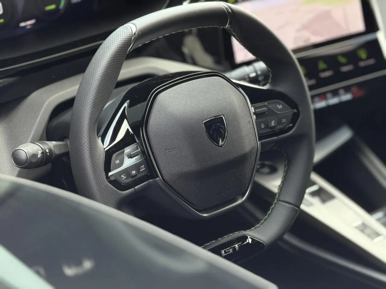 Gros plan sur le volant cuir noir GT avec surpiqûres vert Adamite de la Peugeot 308 Hybrid 2026.