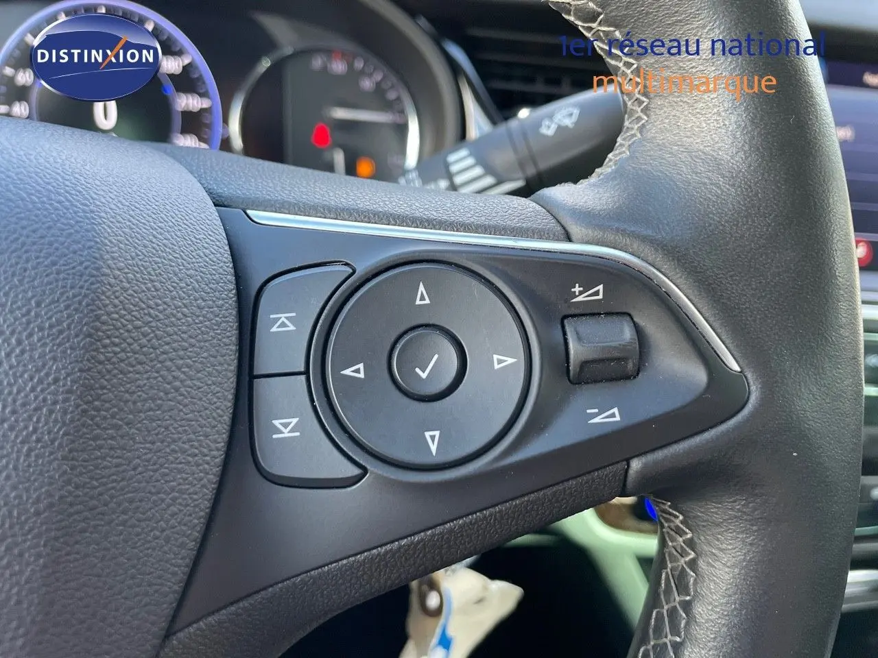 Gros plan sur les commandes au volant en cuir noir de l'Opel Insignia gris minéral métal, tableau de bord en arrière-plan.