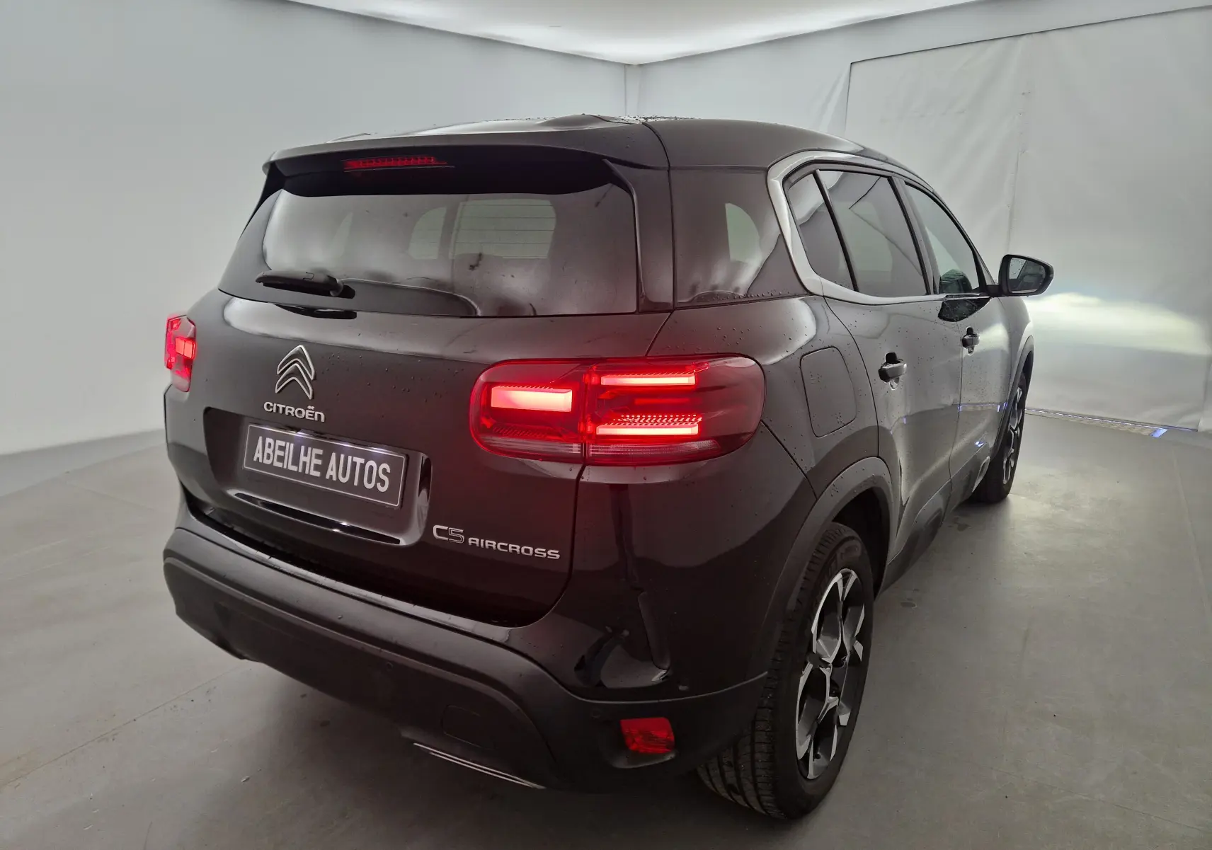 Vue 3/4 arrière droite d'un Citroën C5 Aircross noir 2024 avec feux arrière allumés dans un studio lumineux.