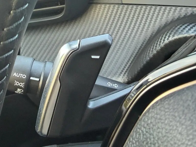 Gros plan sur la commande de régulateur de vitesse au volant, avec tableau de bord effet carbone du Peugeot 2008 rouge Elixir.