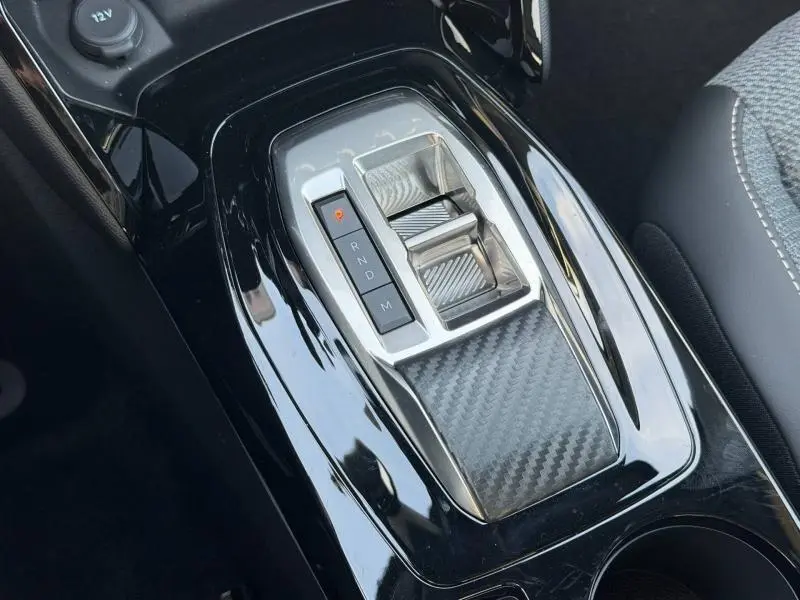 Vue rapprochée de la console centrale noire brillante avec sélecteur de boîte automatique et insert effet carbone dans un Peugeot 2008 rouge.